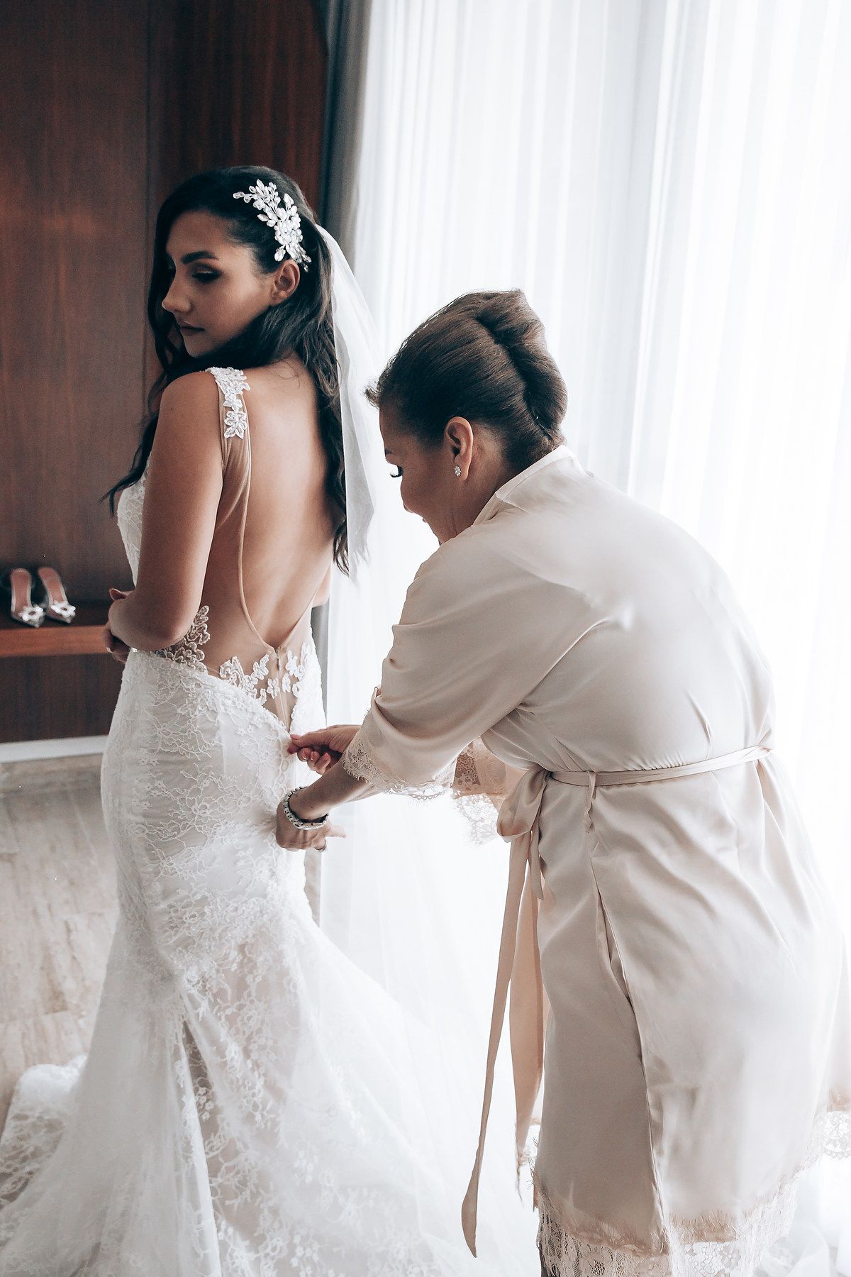 A bride in a white lace wedding dress getting ready with help adjusting her gown.