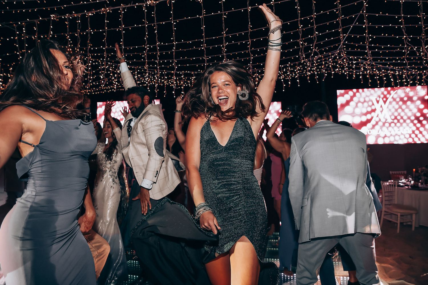 People dancing and celebrating under twinkling string lights at a festive party.
