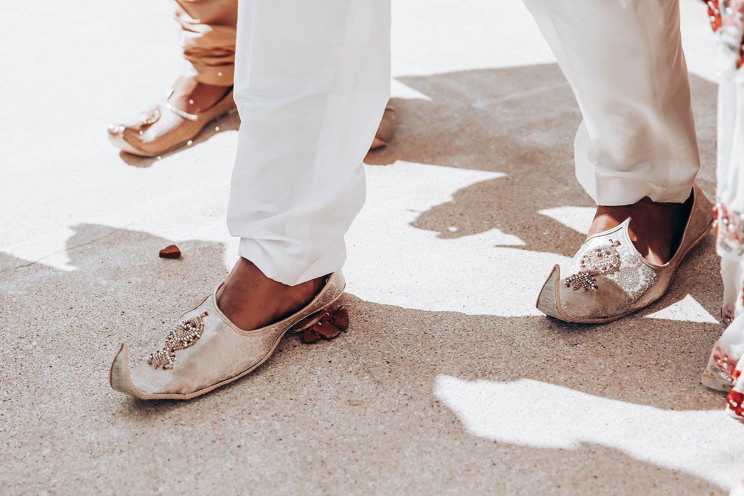 Close-up view of white wedding shoes and dress hems on a sunny outdoor patio.