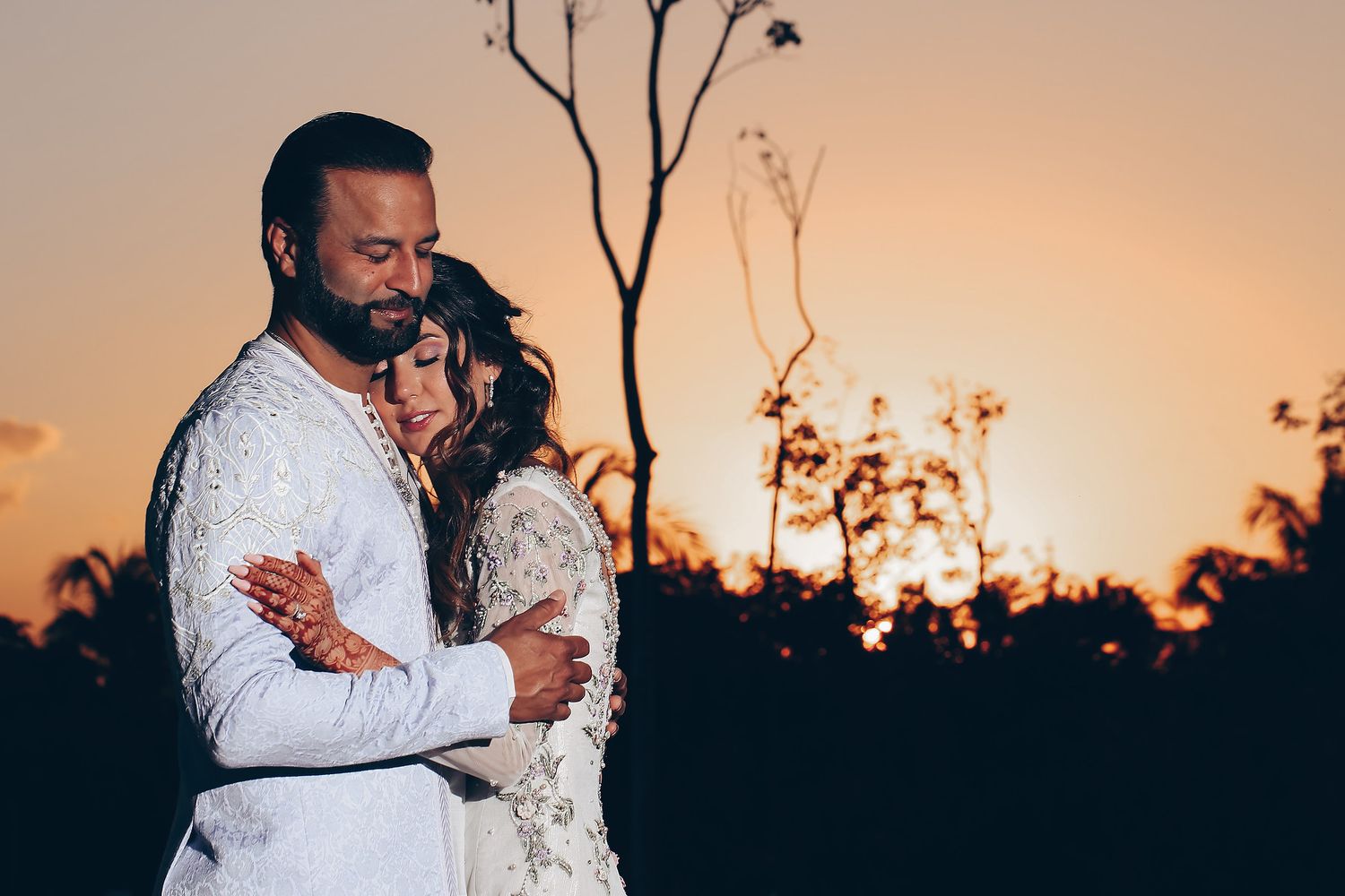 A couple embraces in a romantic sunset photoshoot with silhouetted trees in the background.