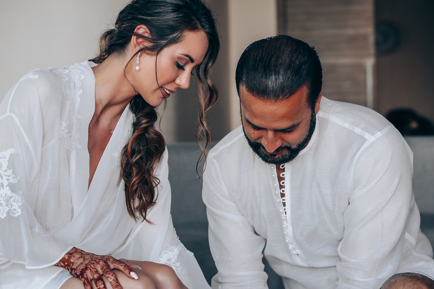 A couple in white outfits signs documents together at a table during what appears to be a special occasion.