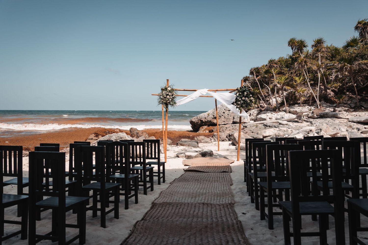 Empty black chairs set up on a wooden deck overlooking a tropical beach.