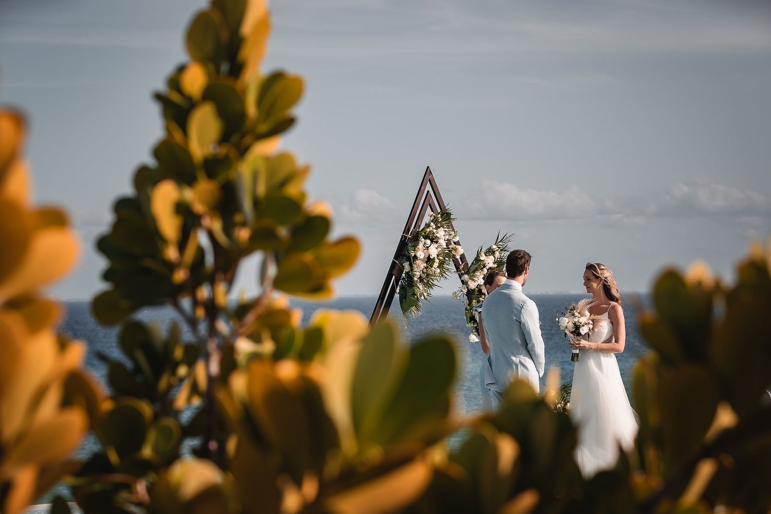 Wedding ceremony arch silhouetted against blue sky with golden foliage in foreground.