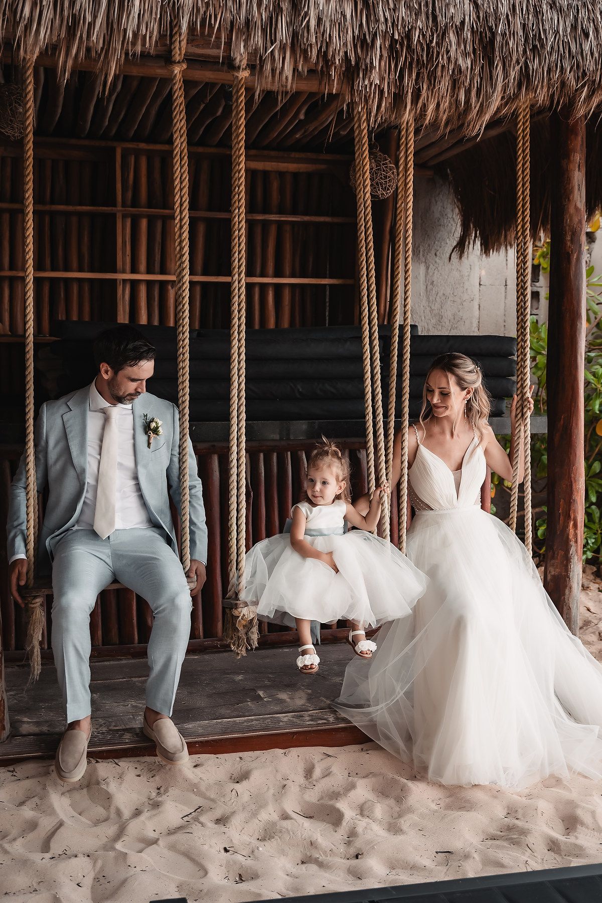 Playful wedding photos on beach swings under a thatched roof palapa.