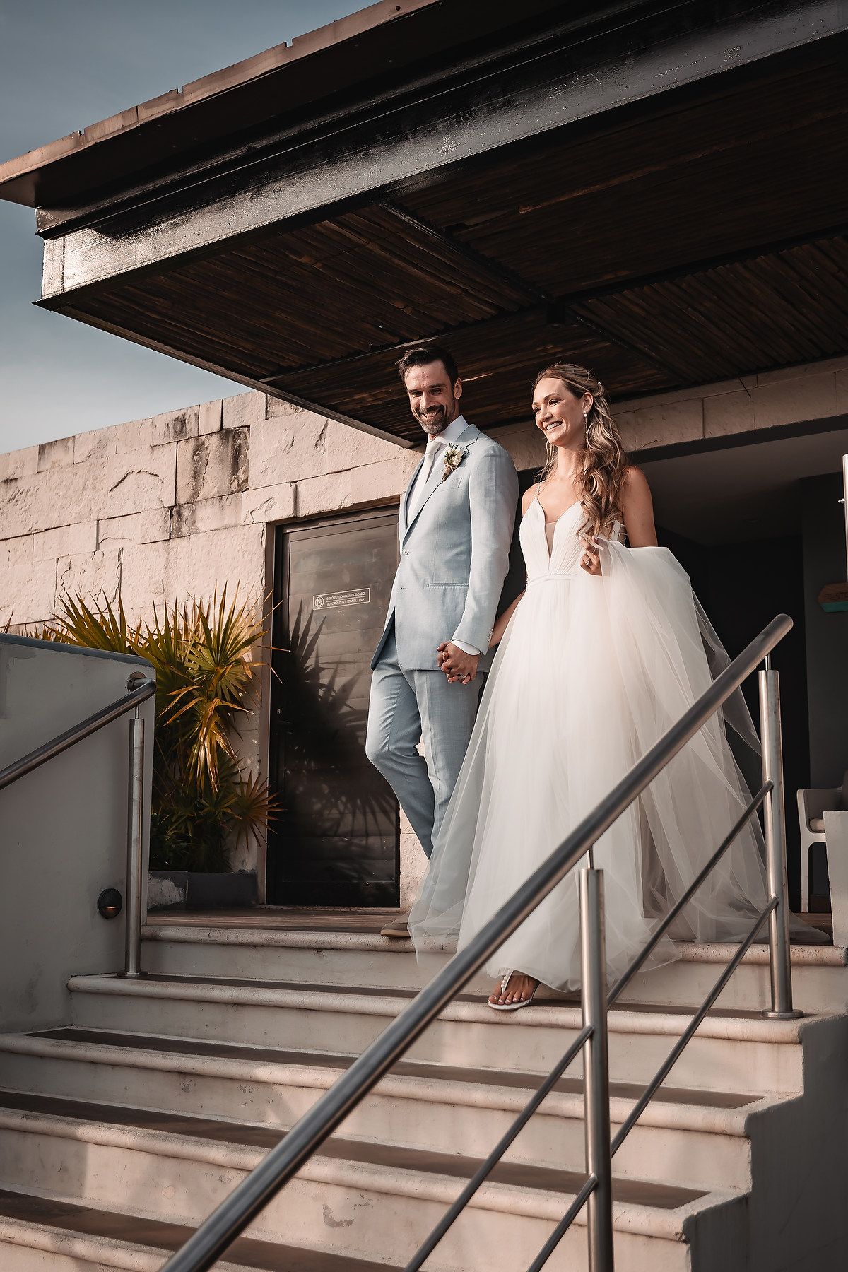 Wedding couple descending modern concrete steps in light-filled outdoor setting.