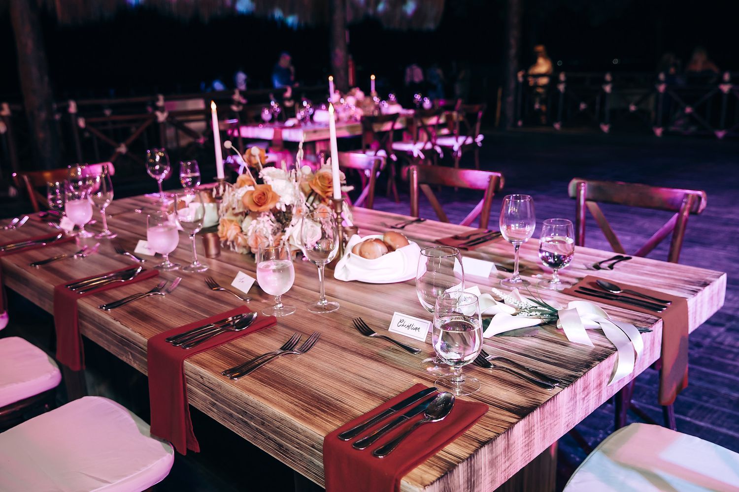 A series of elegant table settings at a wedding reception with purple ambient lighting and wooden table decor.