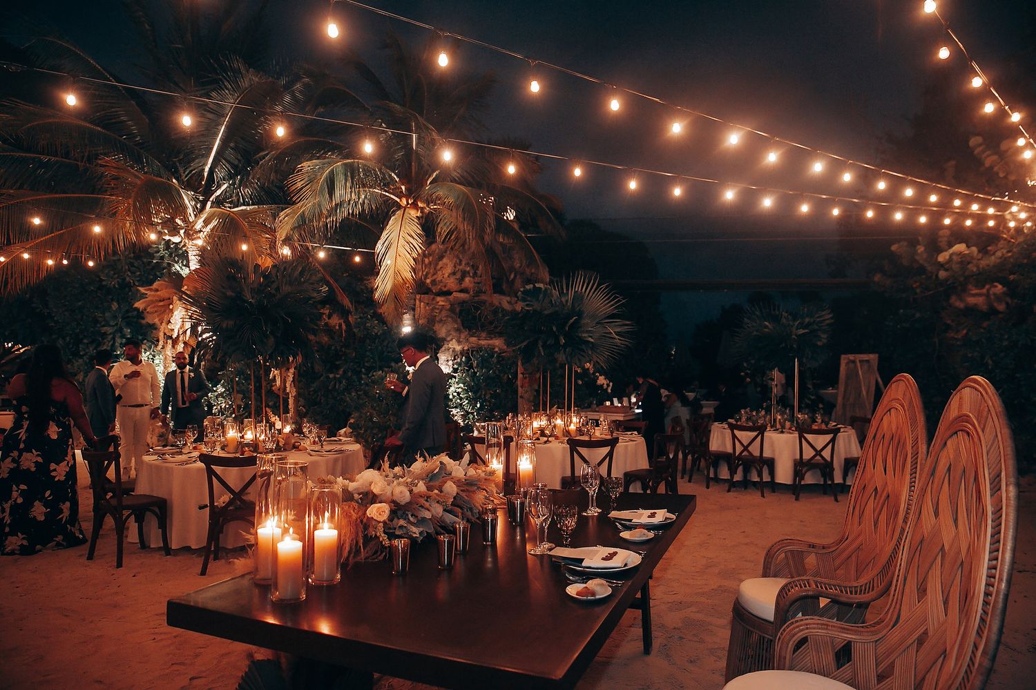 Outdoor wedding reception venue illuminated by warm string lights at dusk.