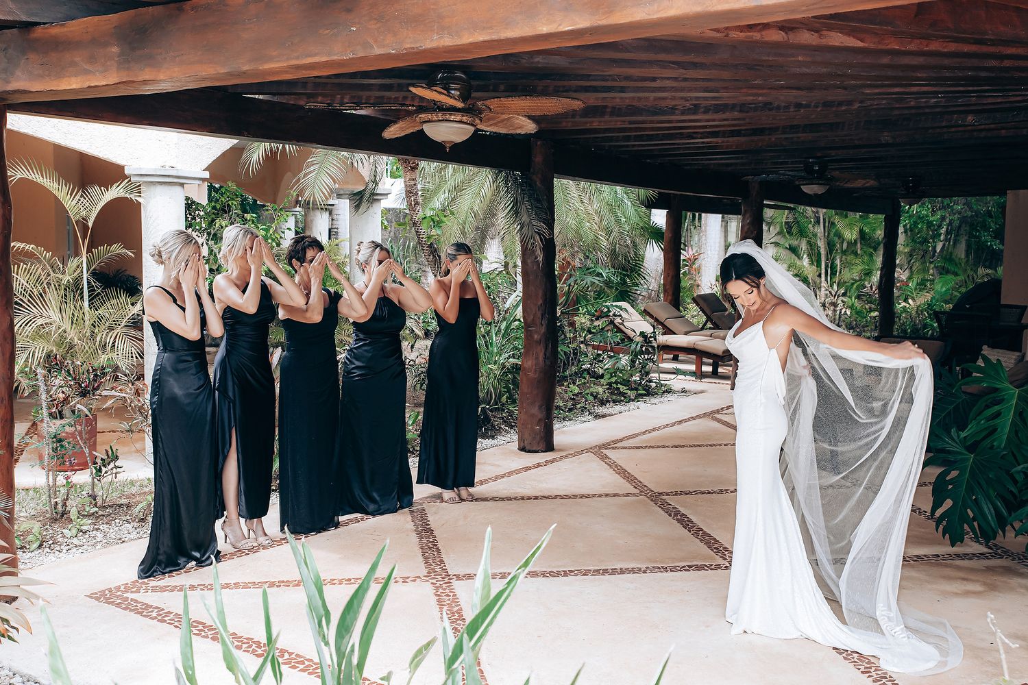 Wedding party in navy dresses poses with bride in white gown on a covered outdoor patio.