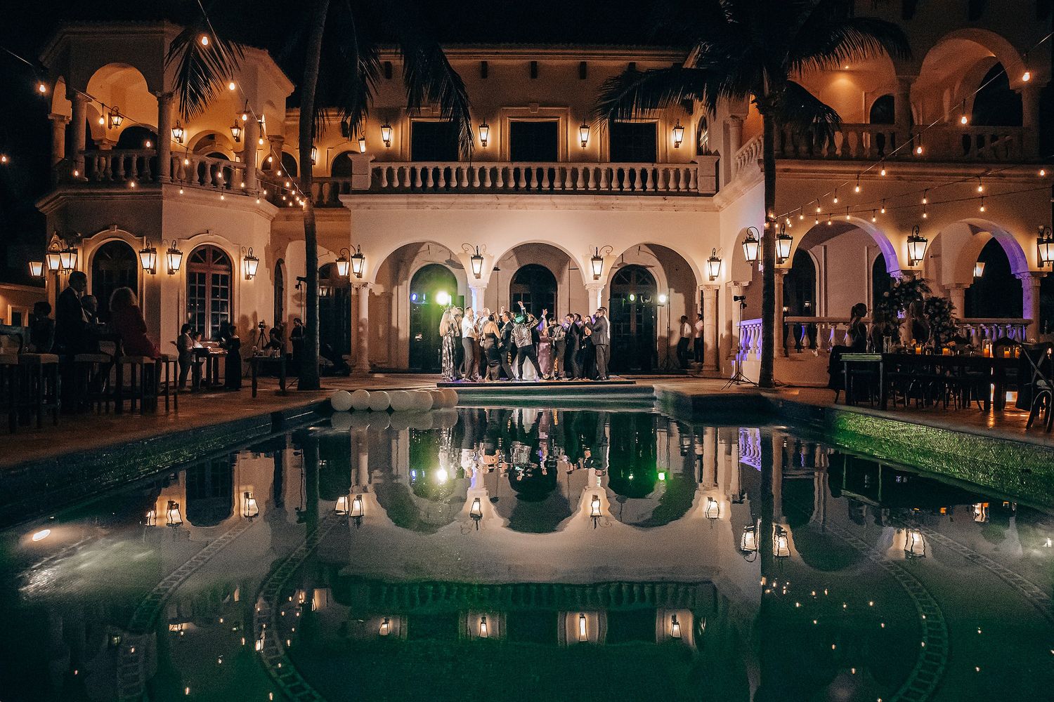 Elegant pool area of wedding venue at night with arched architecture and reflective lighting.