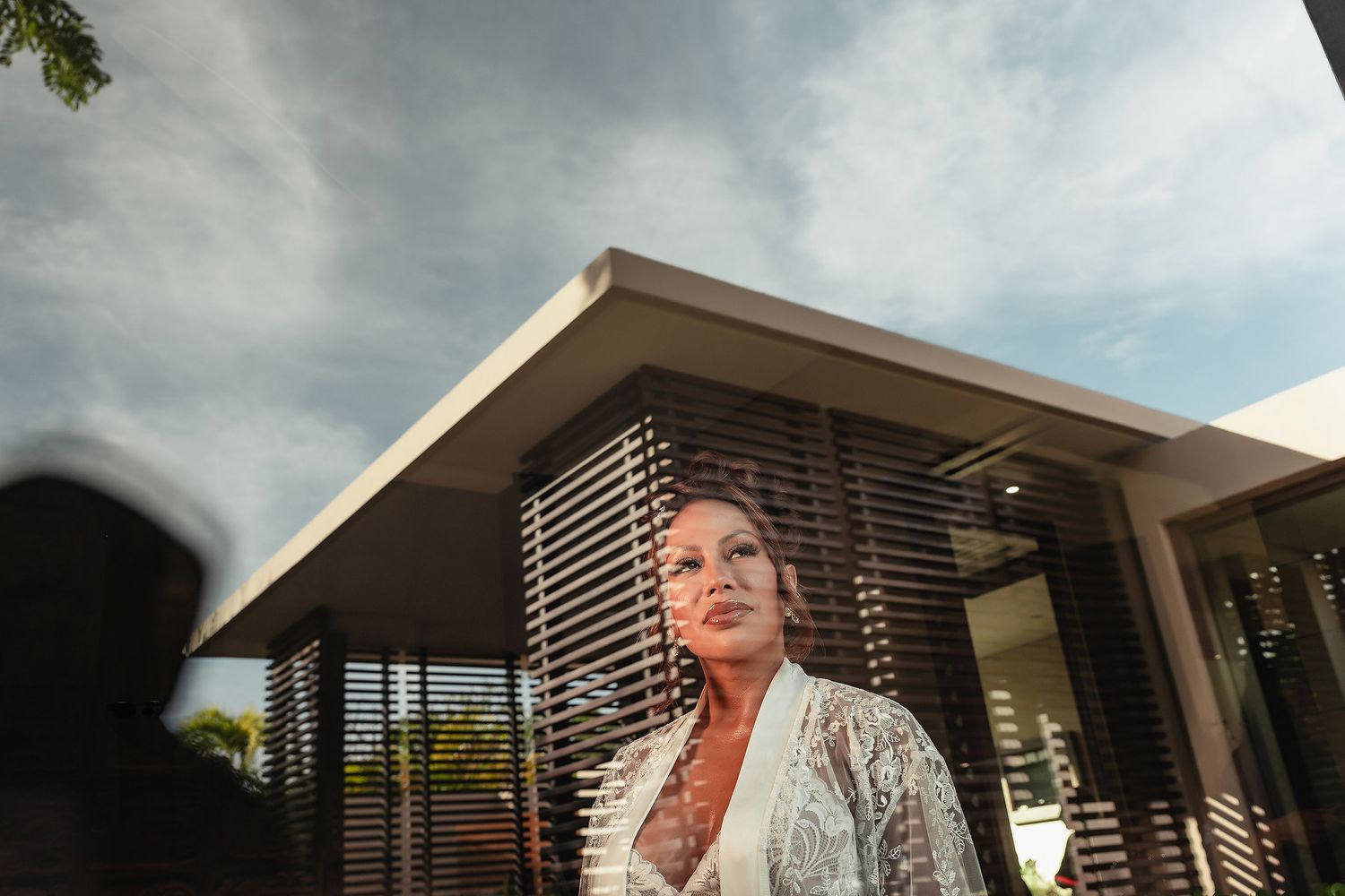 A modern home exterior with horizontal slatted details and an overhanging roof against a cloudy sky.