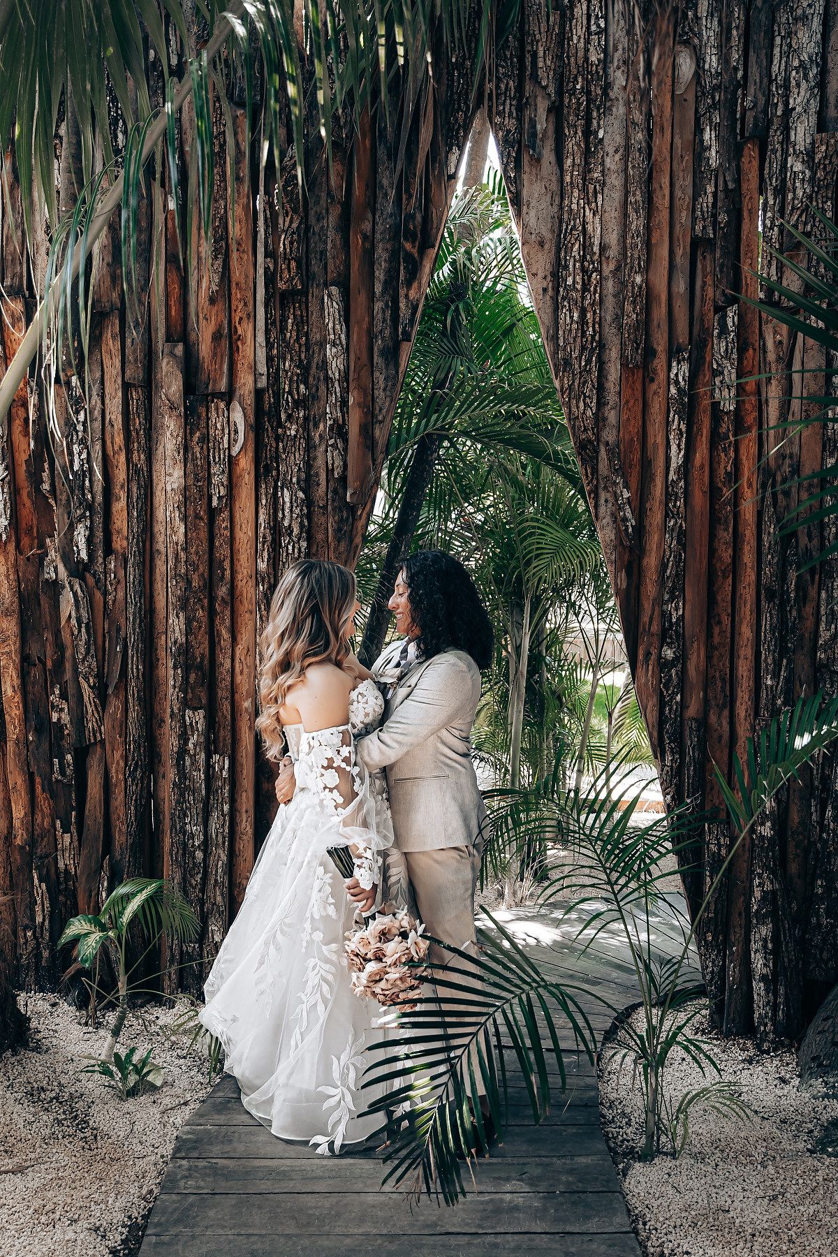 Romantic wedding photos of a couple posing against rustic wooden walls surrounded by tropical palm fronds.