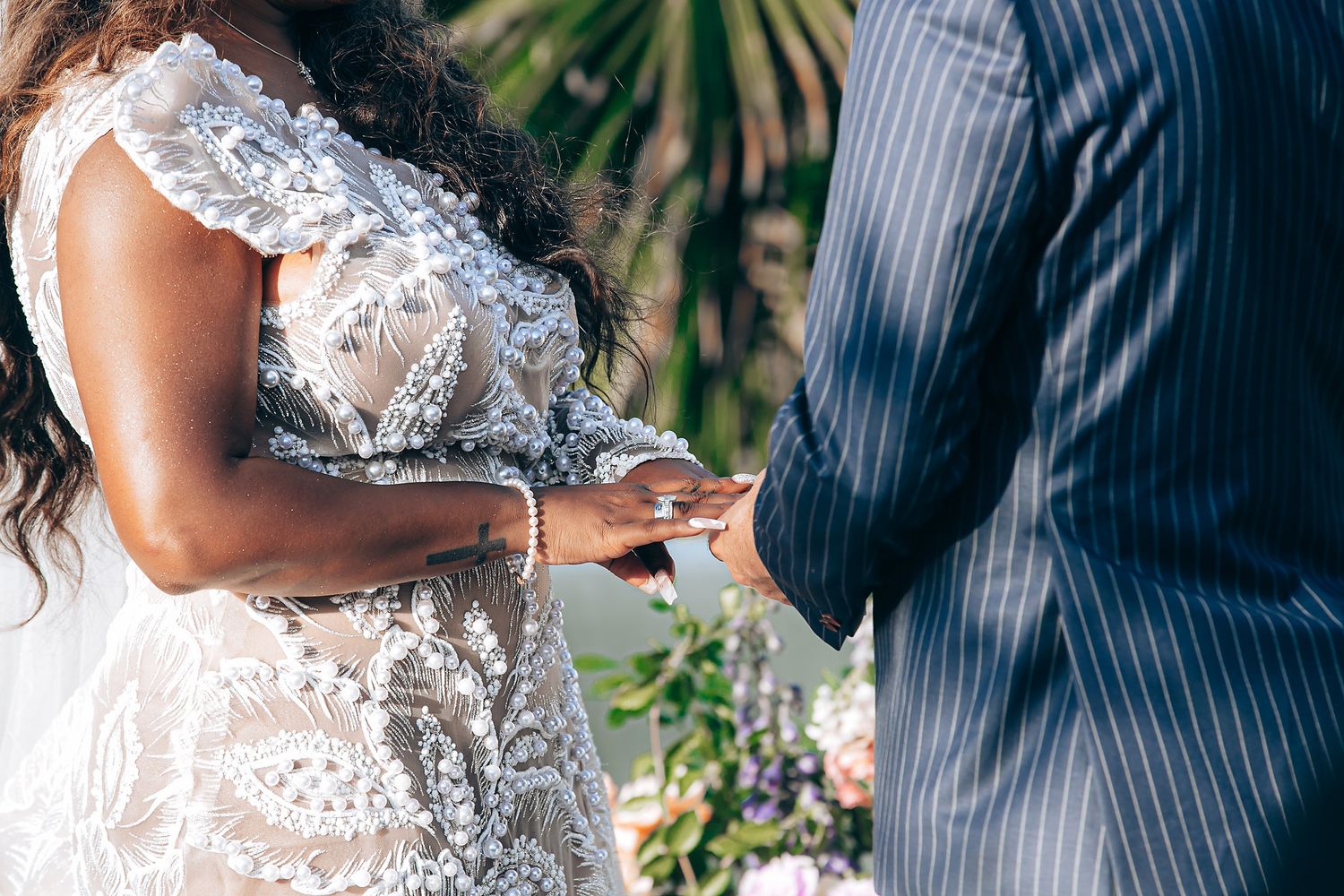 Close-up of wedding ceremony showing hands exchanging rings with lace wedding dress detail in foreground.