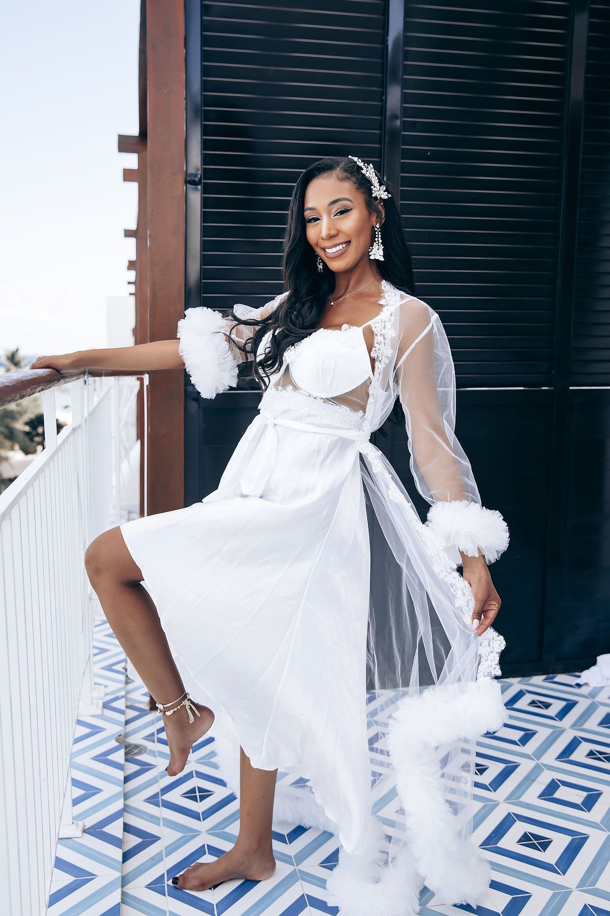 Bride in a flowing white dress poses playfully on a patterned tile floor during a wedding photoshoot.