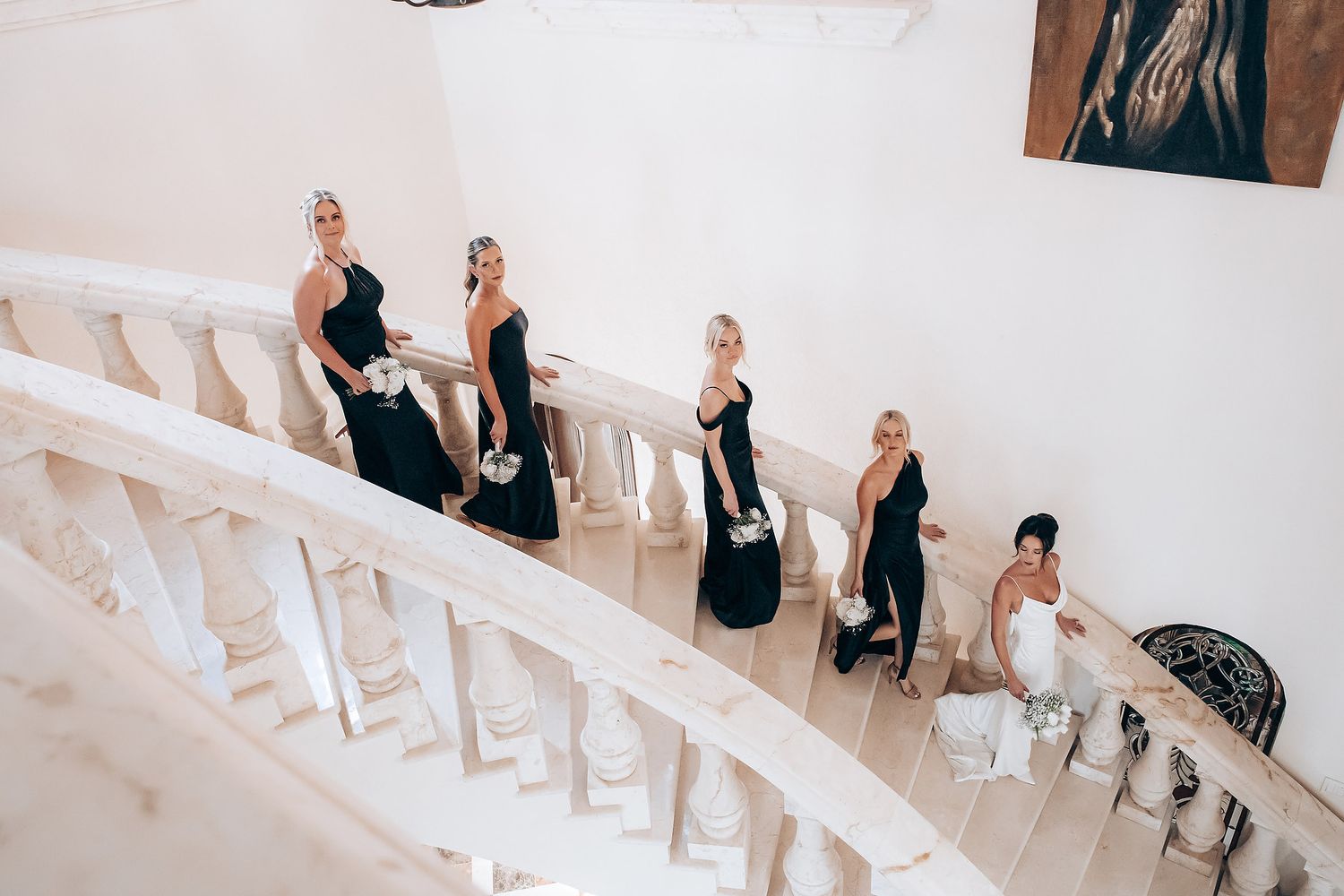 Wedding party in black and white formal attire descends elegant curved white staircase.
