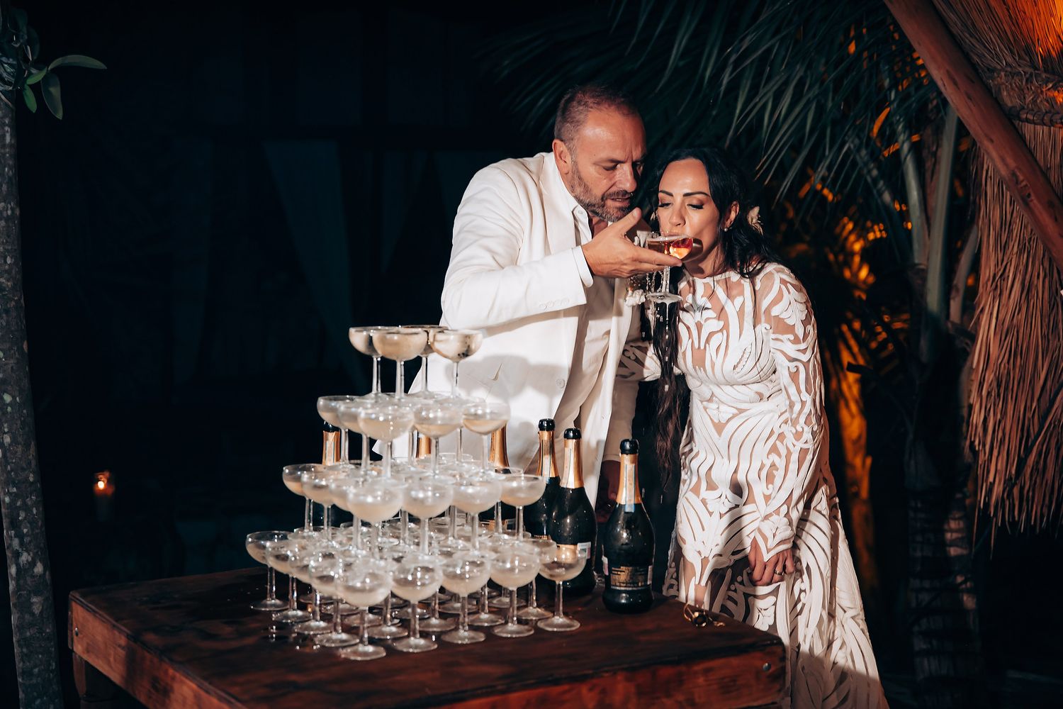 Champagne tower being filled at an elegant evening event with palm trees in the background.