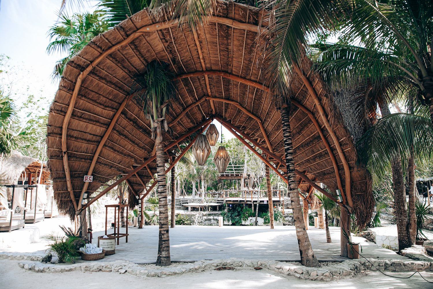 A series of rustic thatched-roof beach huts and palm trees line a tropical shoreline.