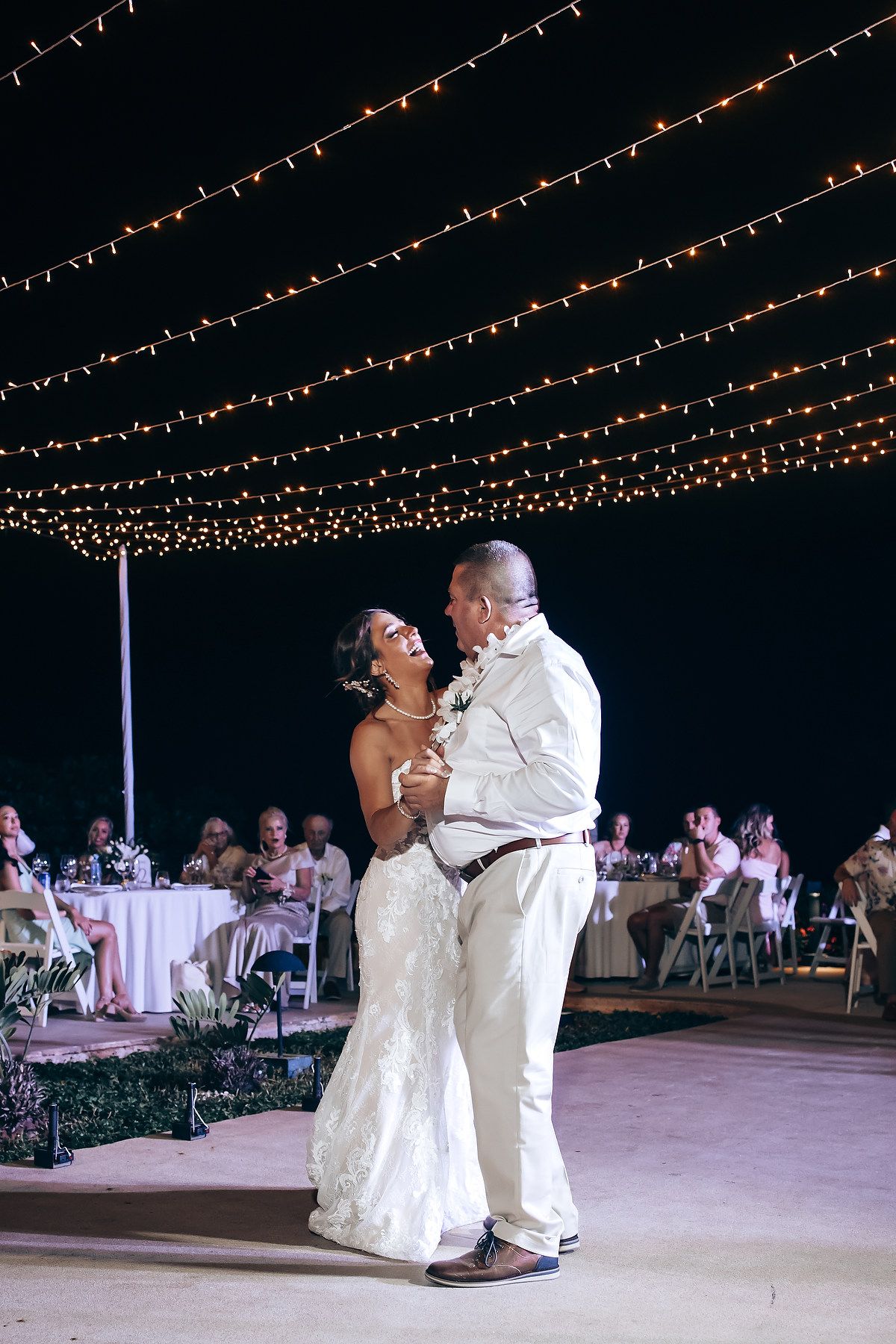Couple shares their first dance under twinkling string lights at outdoor reception.