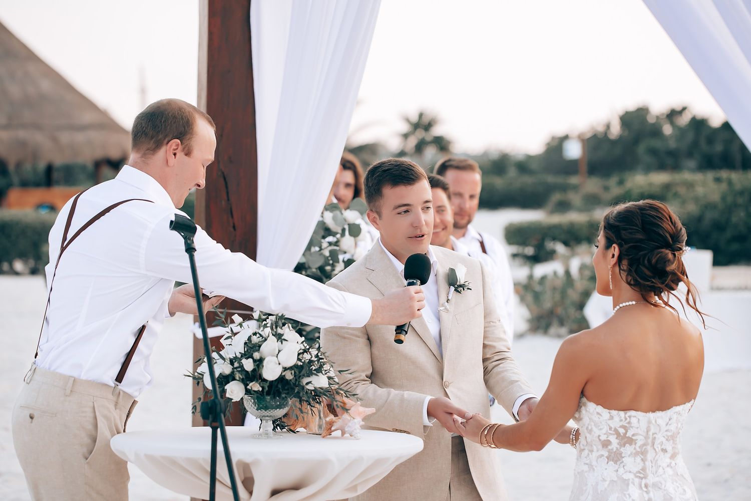 Wedding ceremony moments captured under white draped arch on beach.