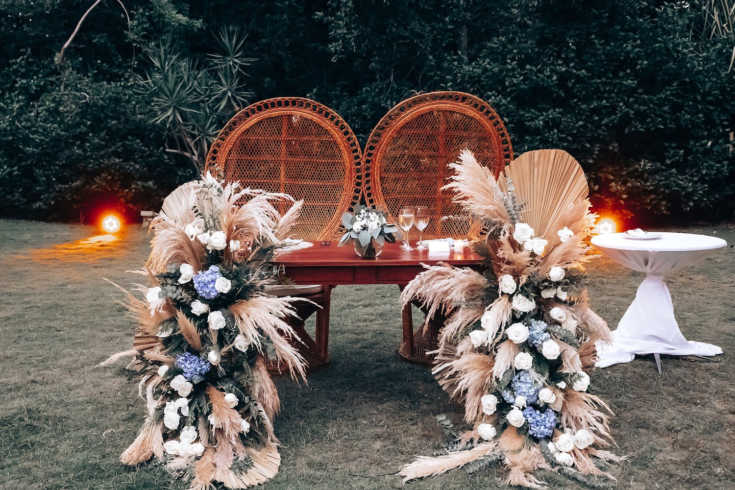 Wedding reception decor with dried pampas grass and blue floral arrangements at night.