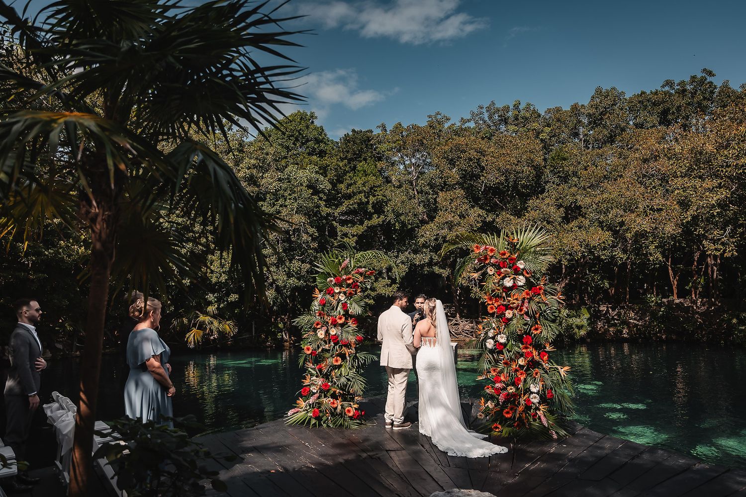 Wedding ceremony location with palm trees and natural water feature in background.