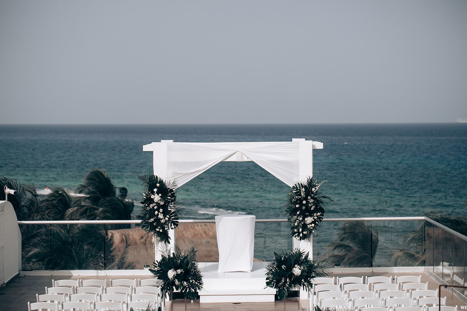 Beachfront wedding venue with white pergola and chairs facing the ocean horizon.