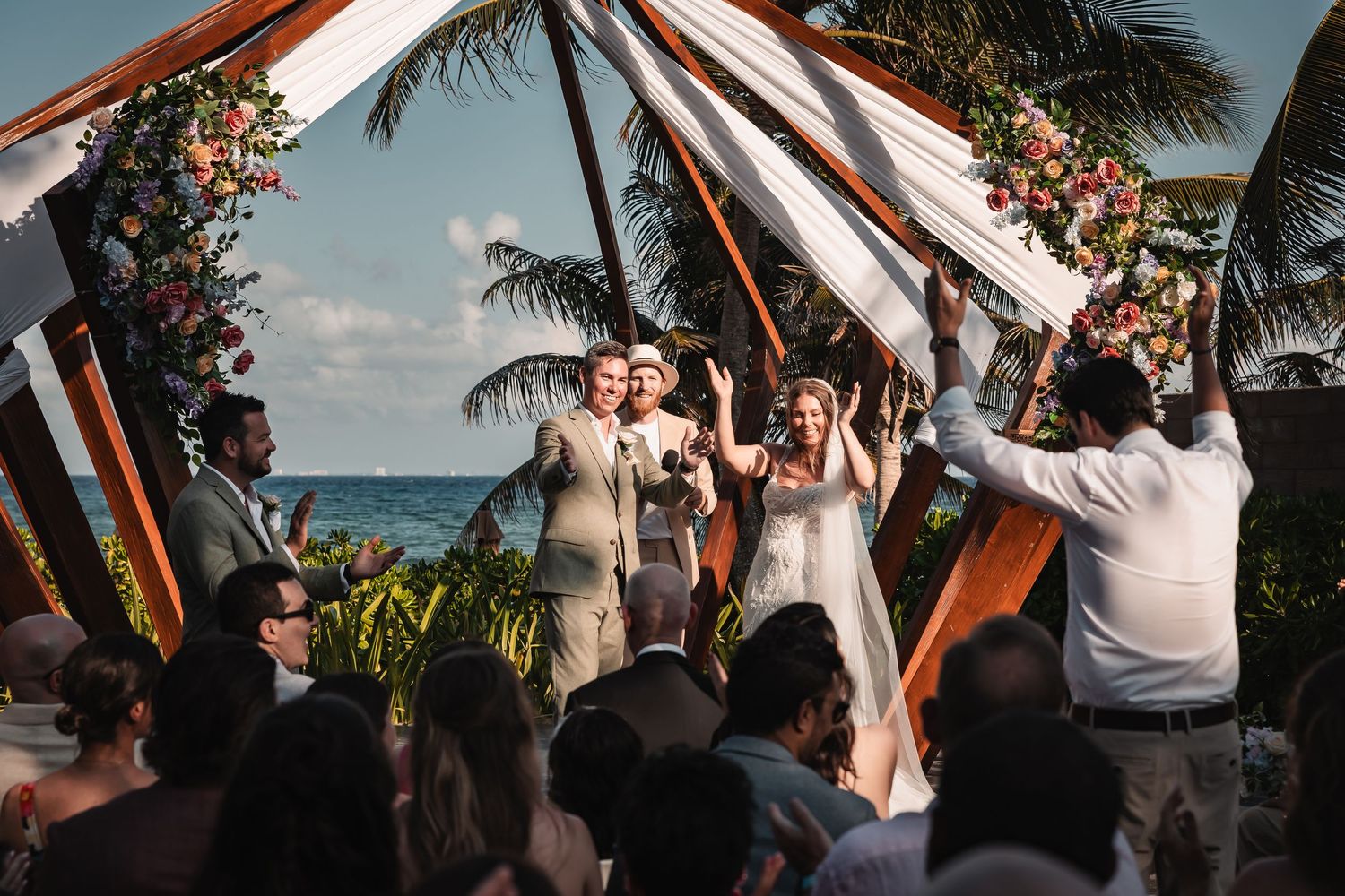 Outdoor beach wedding ceremony with white chairs and tropical palm trees during golden hour.