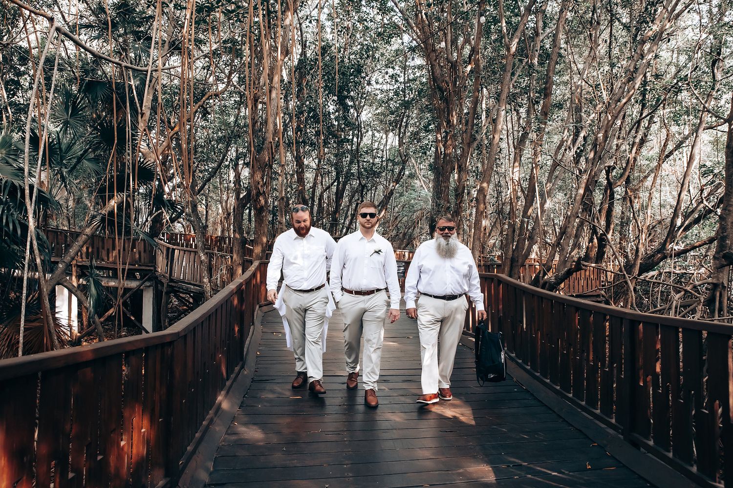 People in white attire walking along wooden boardwalk through natural setting.