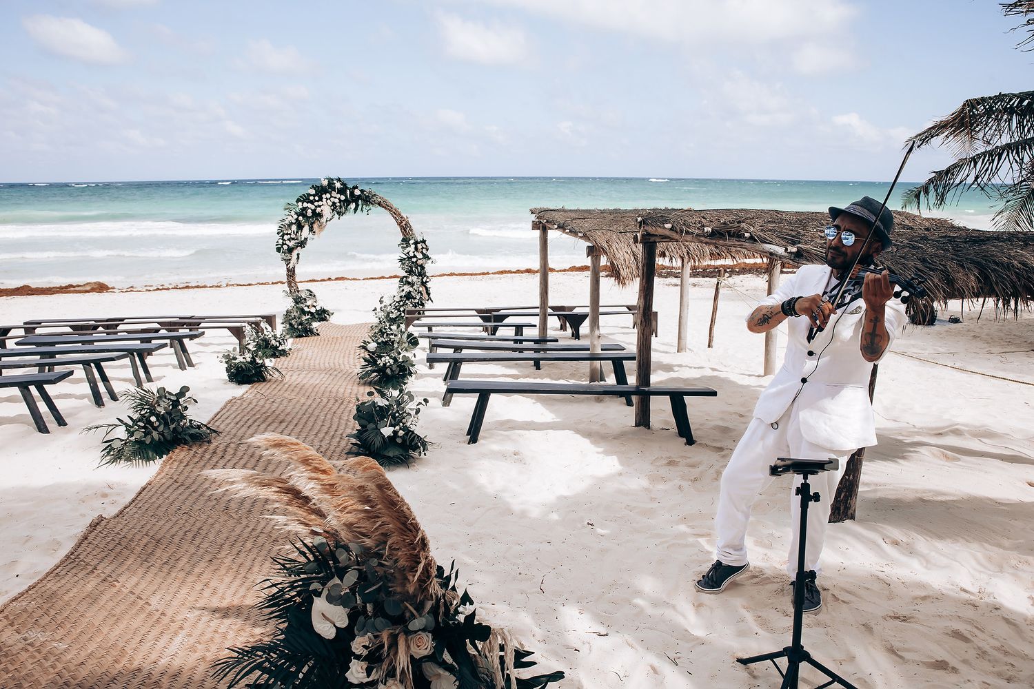 Beach wedding ceremony setup with rustic wooden benches and a floral arch overlooking the ocean.