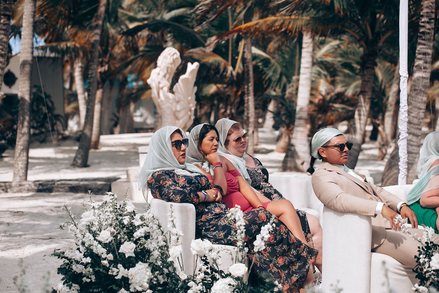Tropical beach wedding venue decorated with white floral arrangements and palm trees.