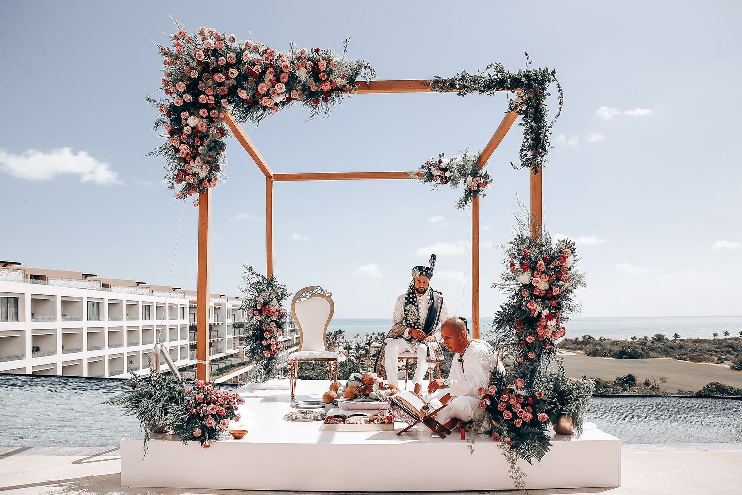 Wooden wedding arch decorated with pink flowers frames an oceanfront view.