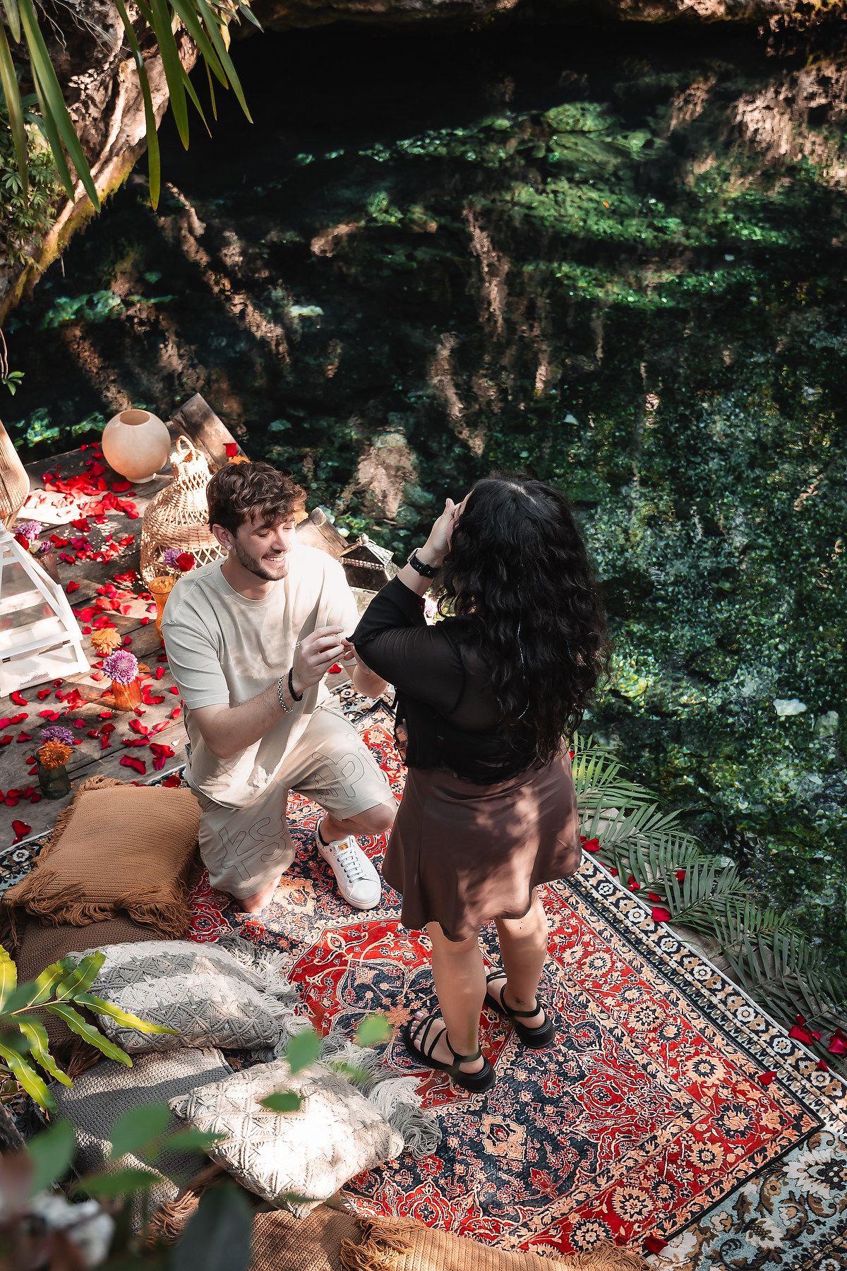 Romantic picnic setup with a red carpet and decorations beside a natural cenote.
