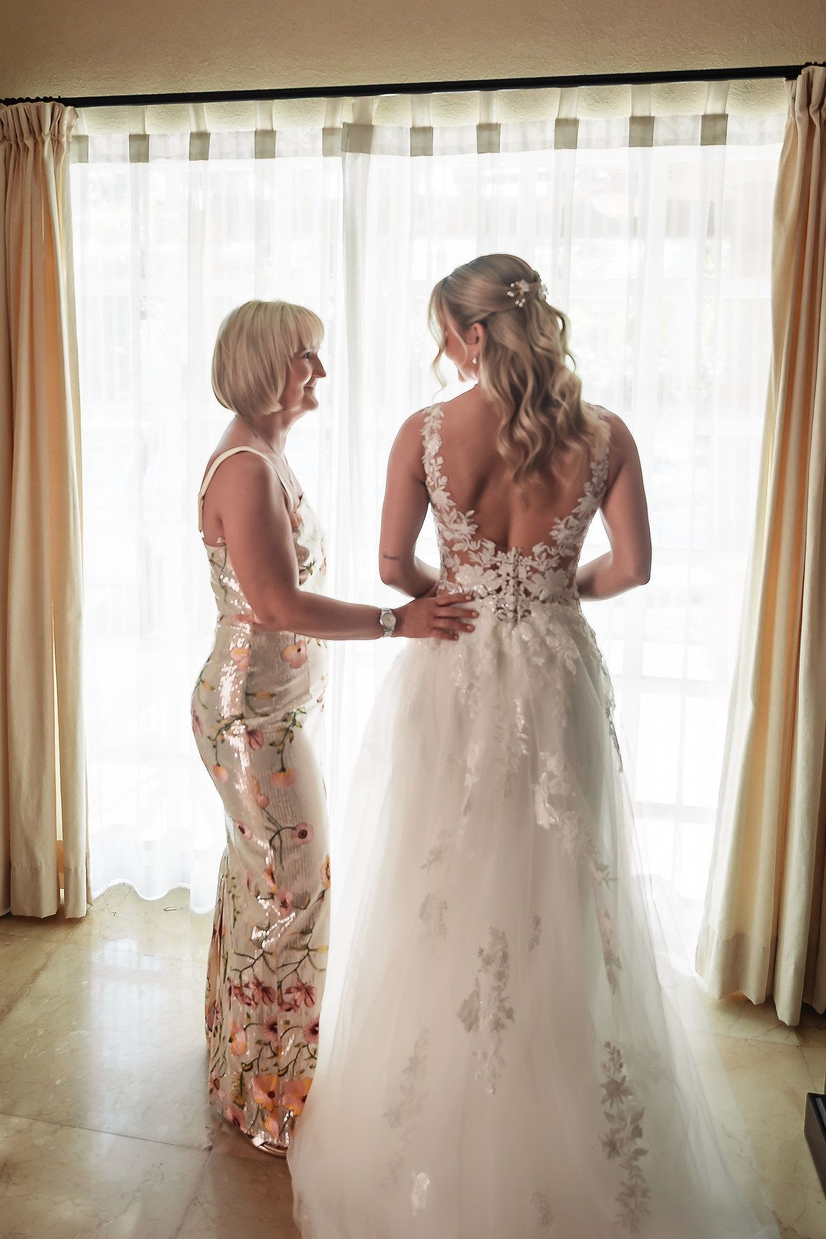 A wedding dress with intricate lace details is being fitted in a bright indoor setting.