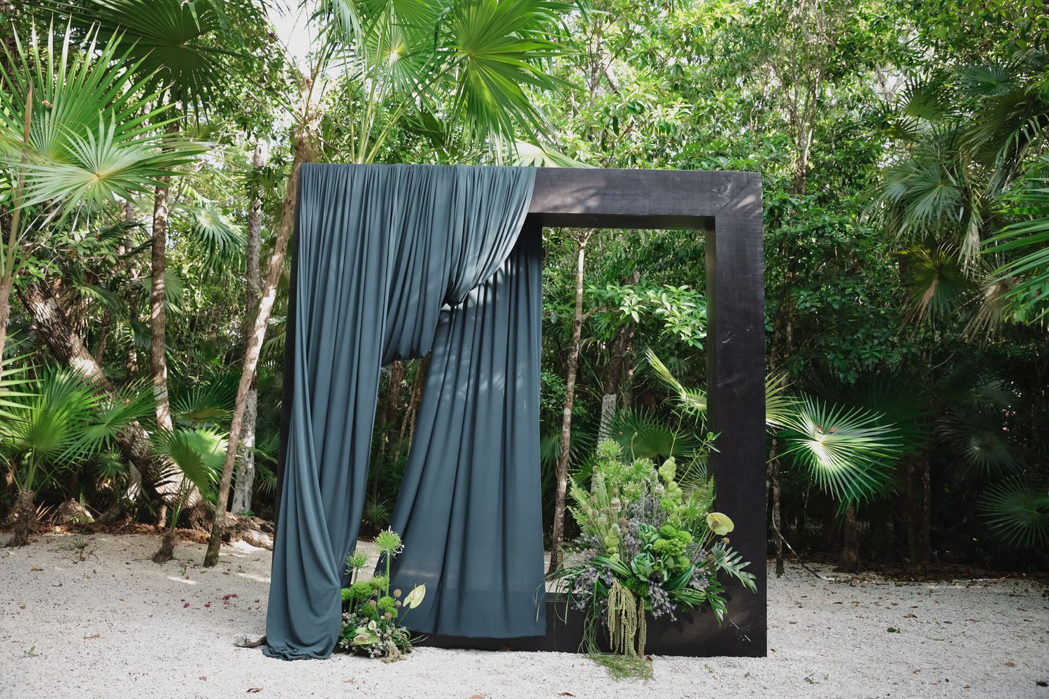 Elegant dark wooden arch with teal draping and tropical greenery in outdoor jungle setting.
