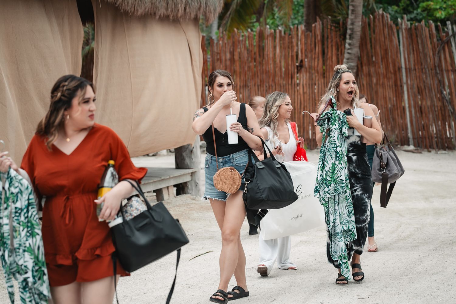 Group of women in summer outfits walking on a tropical beach resort path.