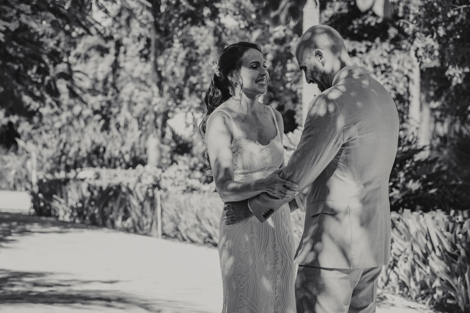 Black and white photo of a bride and groom sharing a tender moment outdoors, surrounded by lush trees on their wedding day.