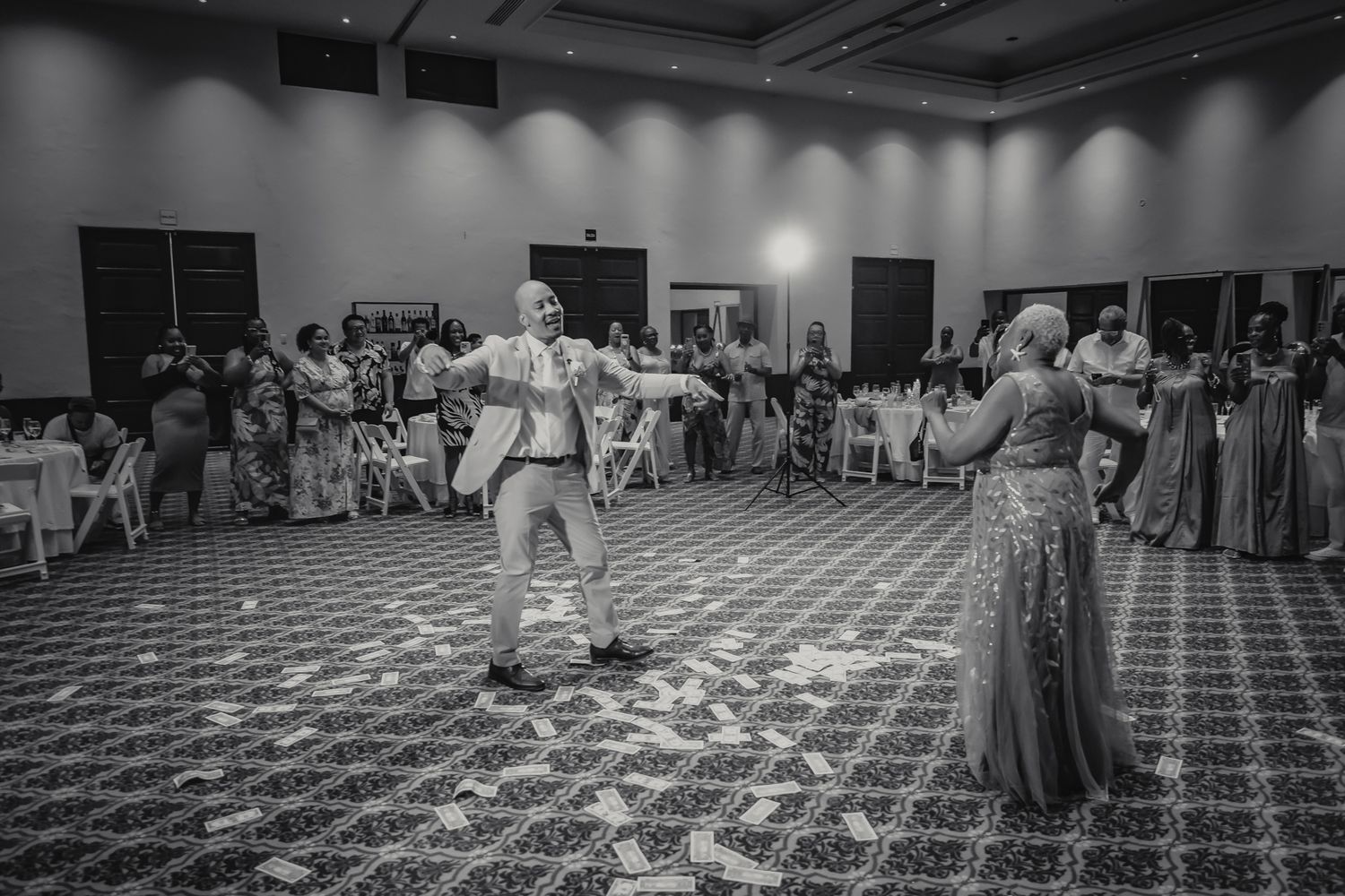 Black and white photo of a couple sharing a first dance at their wedding reception in an elegant ballroom.