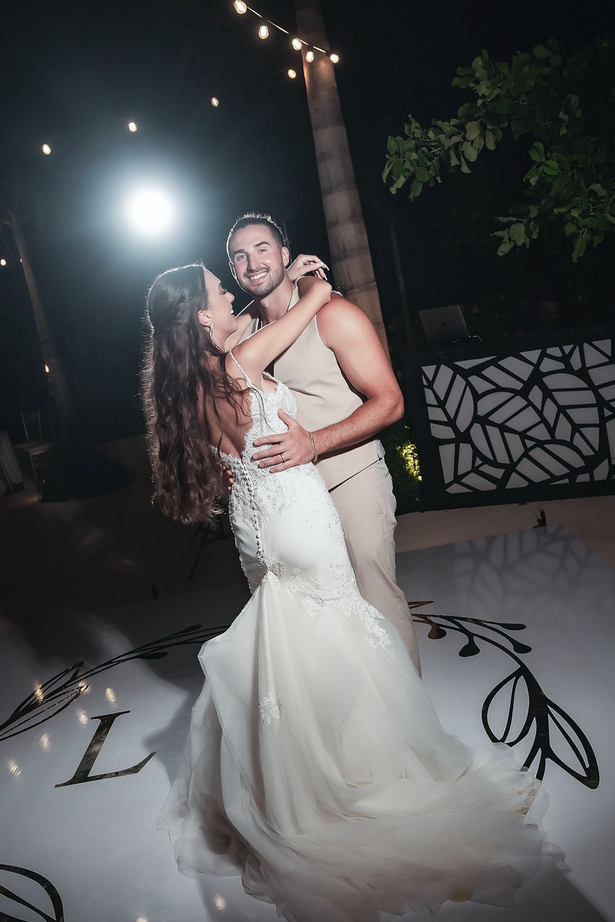 Bride and groom share their first dance on a white dance floor with monogram lighting at an outdoor wedding reception.