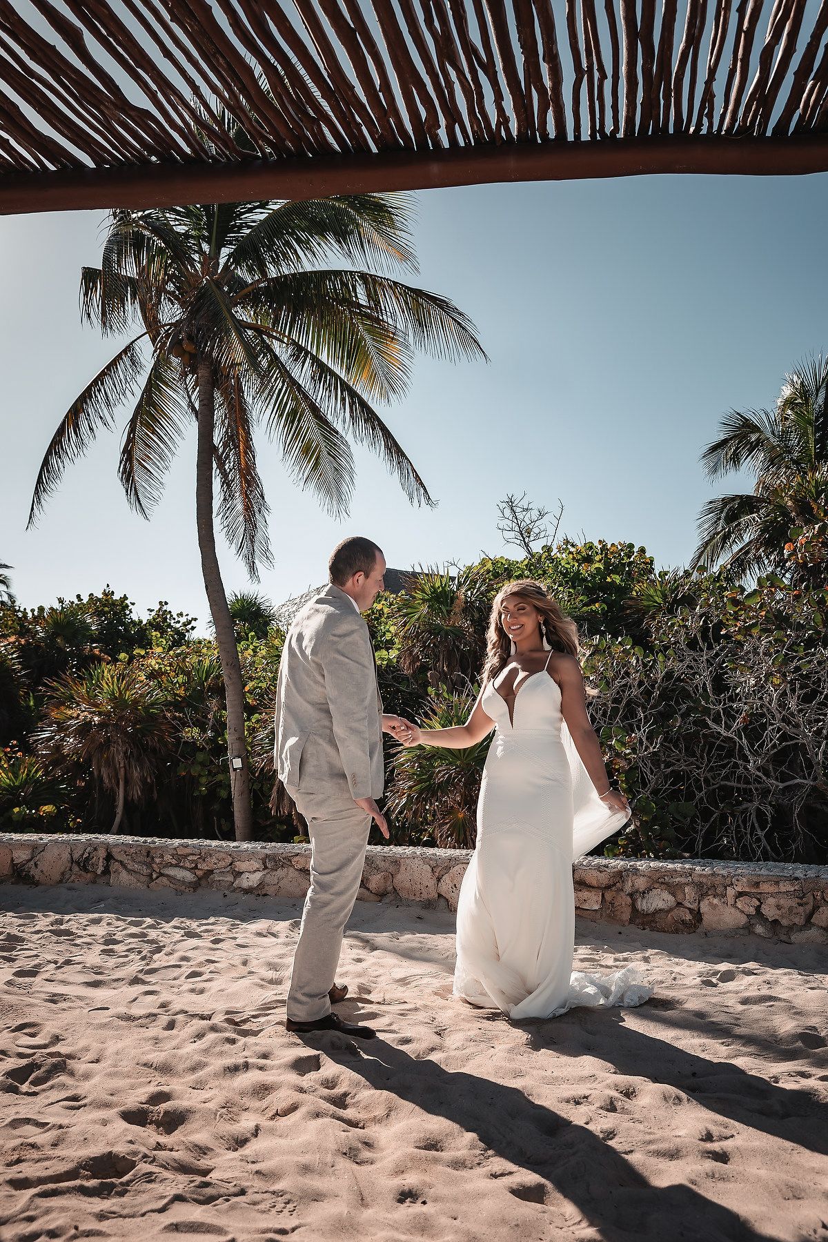 Bride and groom share a romantic first look moment on sandy beach with tropical palm trees at destination wedding.