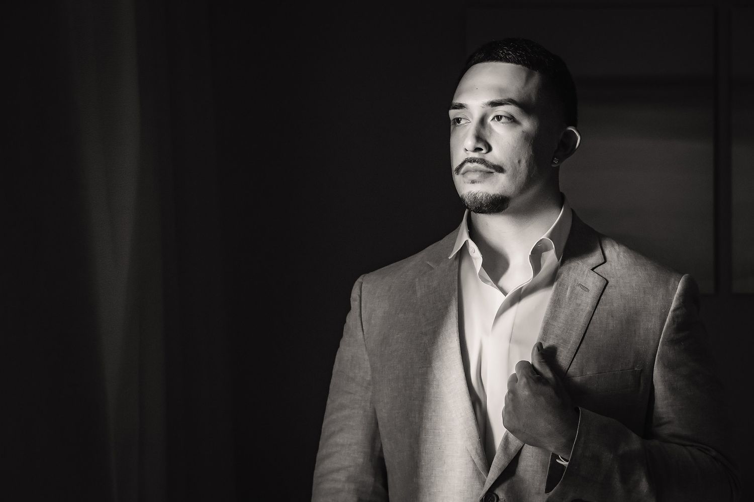 Black and white portrait of a young man in a suit jacket, looking away dramatically in moody lighting.
