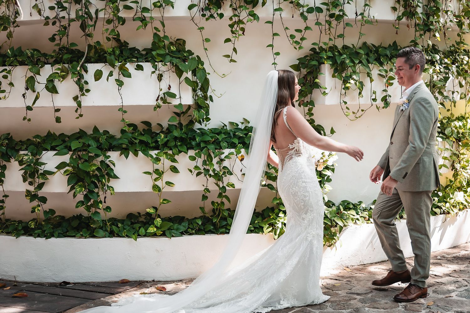 Bride and groom share a tender first look moment in front of a lush ivy-covered white wall.