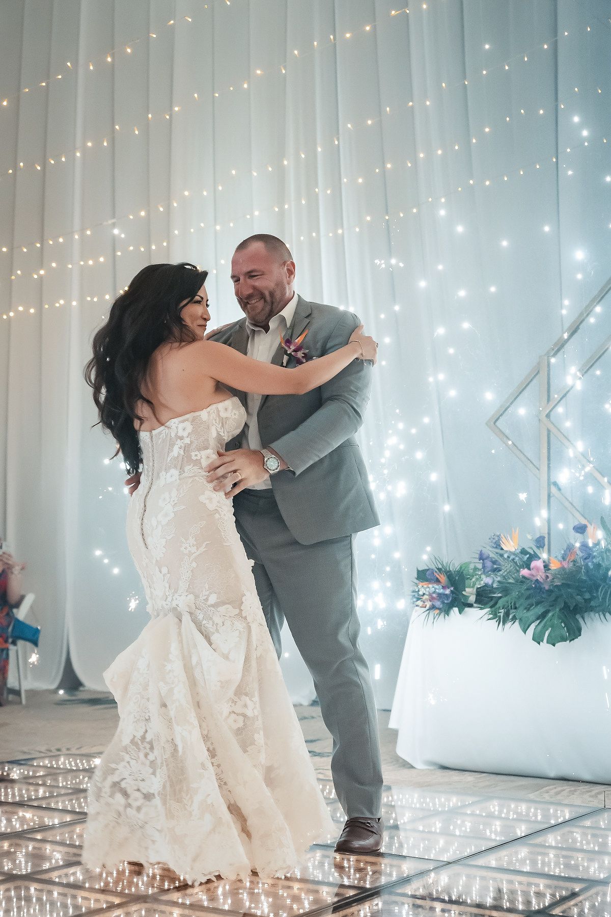 Bride and groom share their first dance on a mirrored floor surrounded by twinkling fairy lights at their wedding reception.