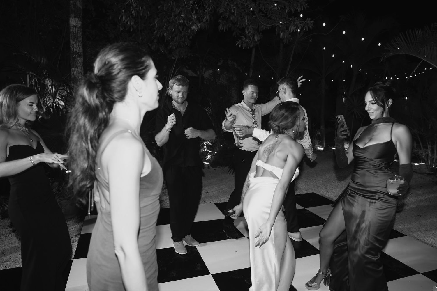 Guests dancing on checkered black and white dance floor at elegant outdoor evening wedding reception.