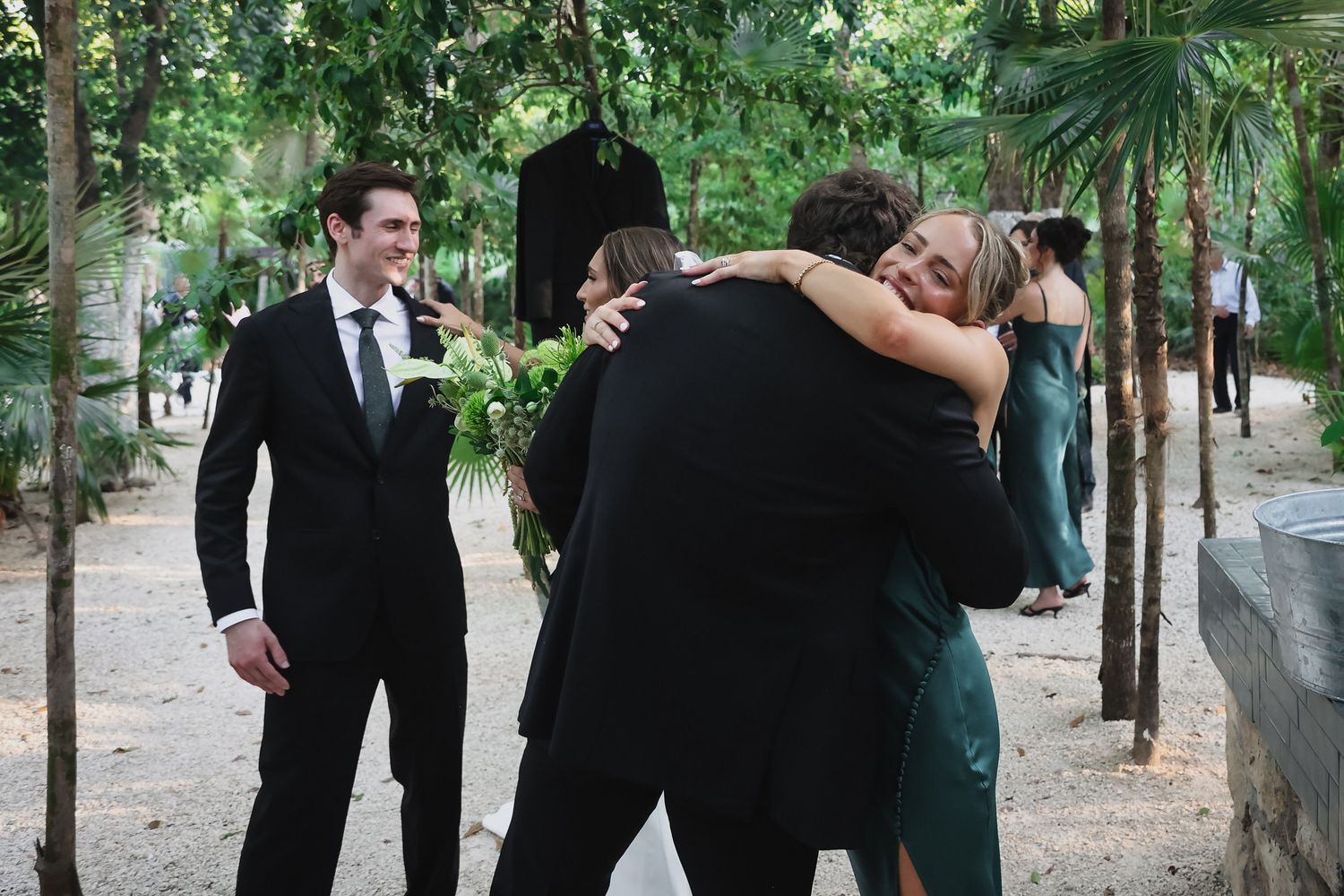 Guests hugging and celebrating at an outdoor wedding reception surrounded by lush tropical greenery.