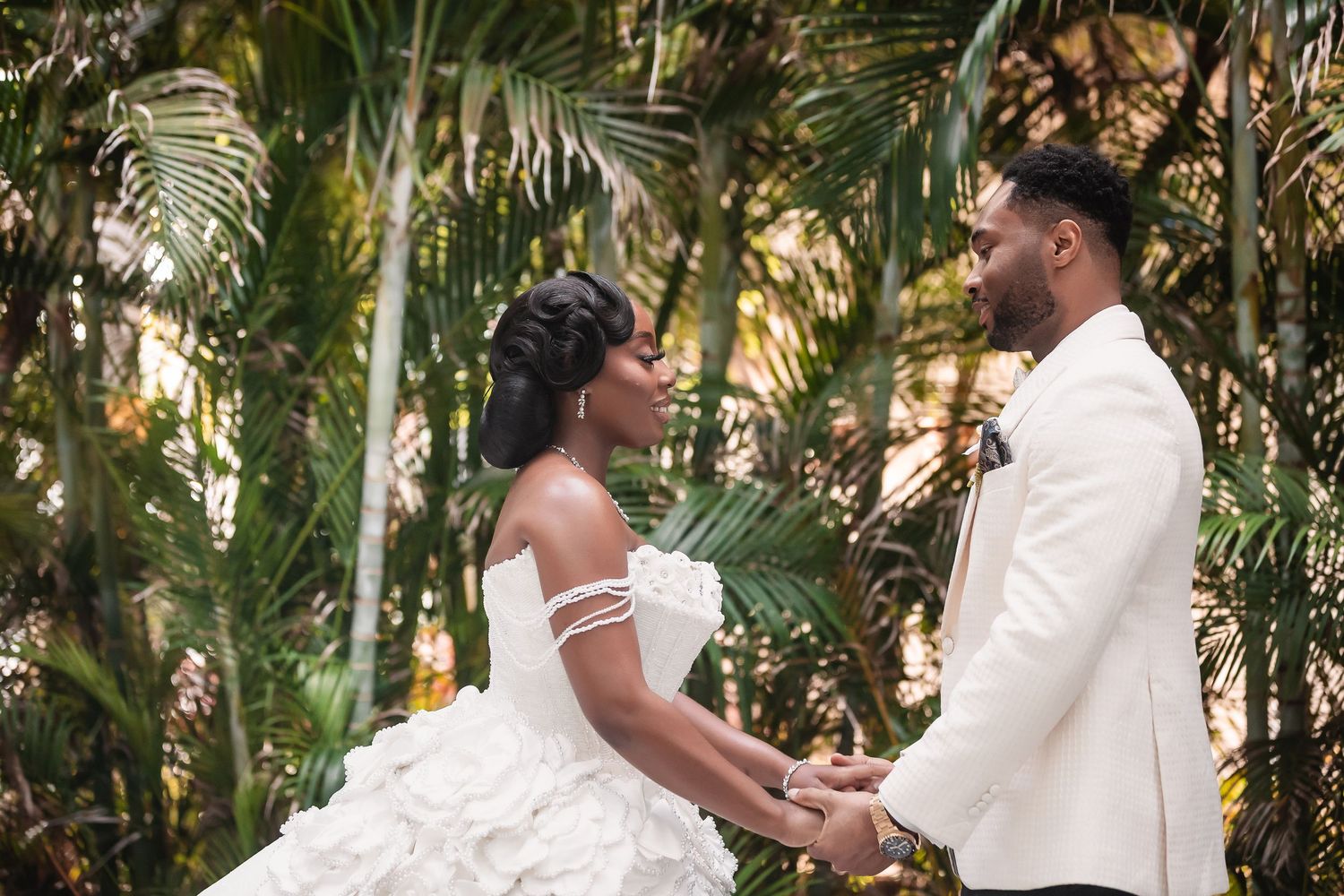 A couple shares a romantic moment in a tropical garden setting wearing matching white attire.