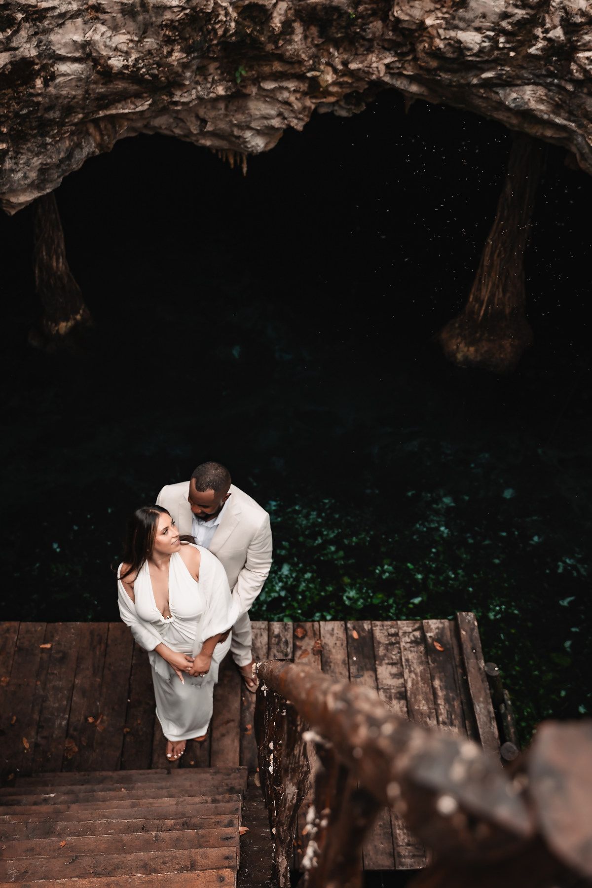 Overhead view of couple on wooden platform at entrance of dramatic cave cenote.