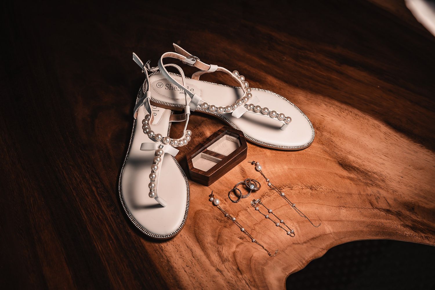 Delicate bridal accessories including jeweled sandals and sparkling hair pieces arranged on wooden surface.