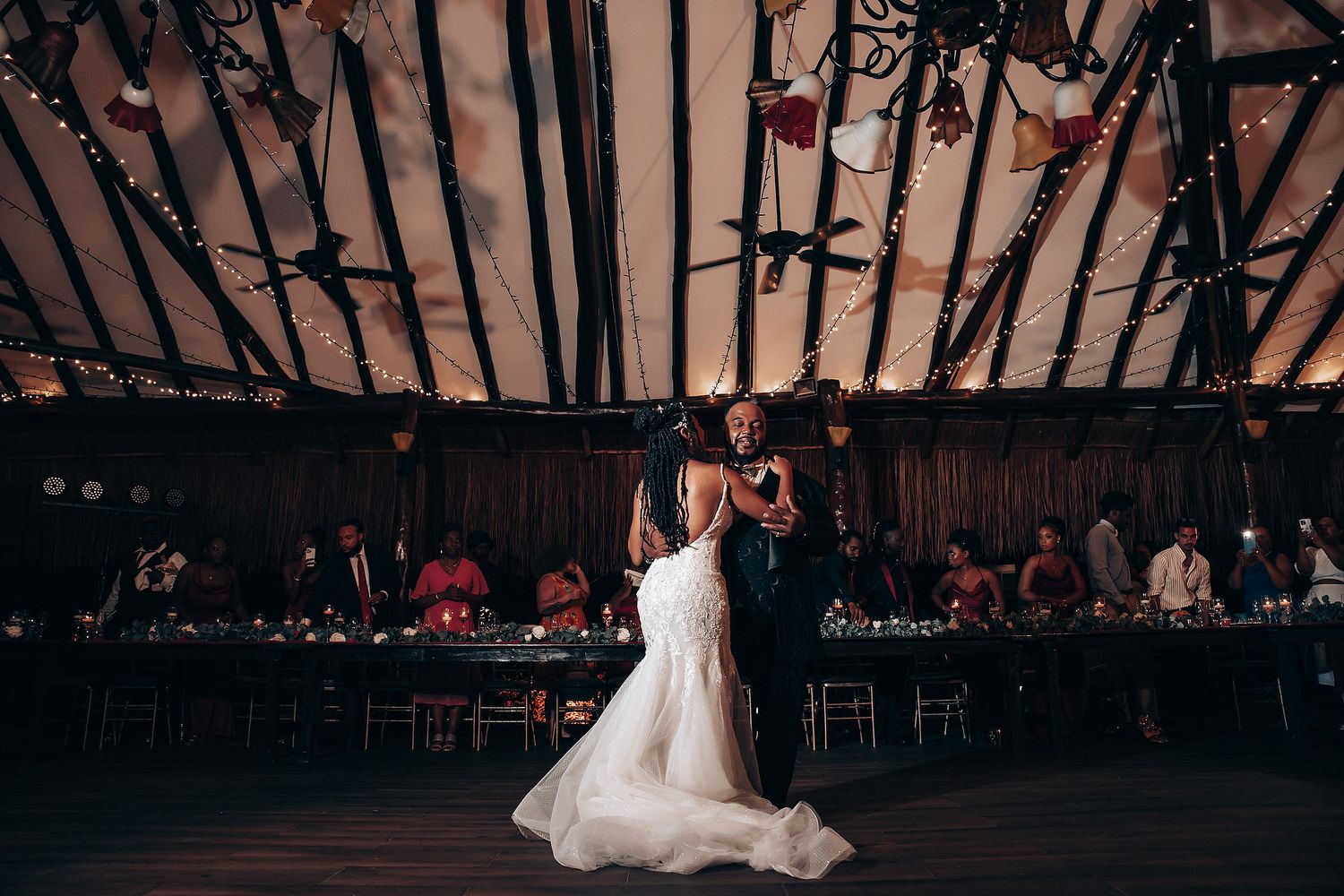 A bride and groom share their first dance surrounded by guests at a rustic barn wedding reception.