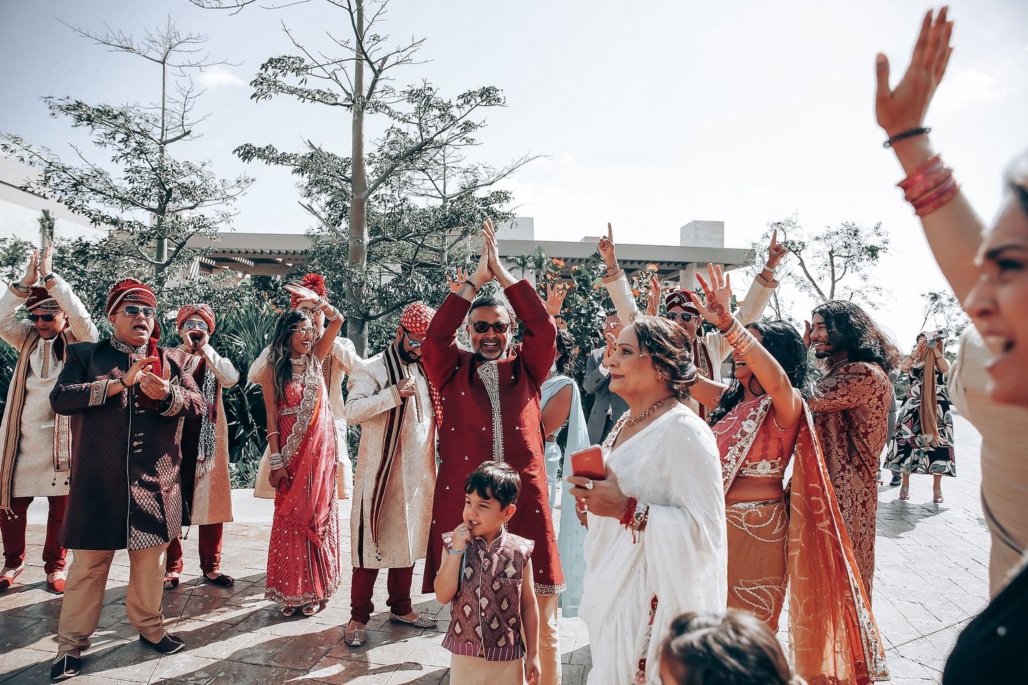 Wedding guests celebrate outdoors by raising their arms and cheering during a joyful reception moment.