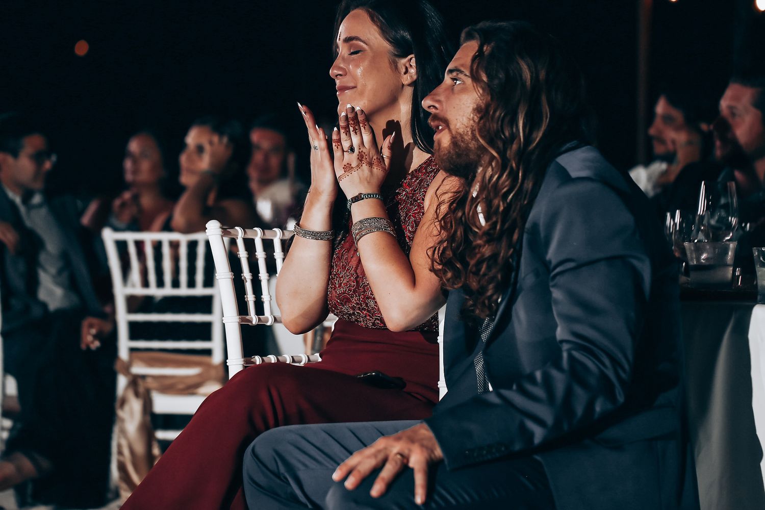 Wedding guests react with joy and excitement during an emotional moment at an indoor reception celebration.