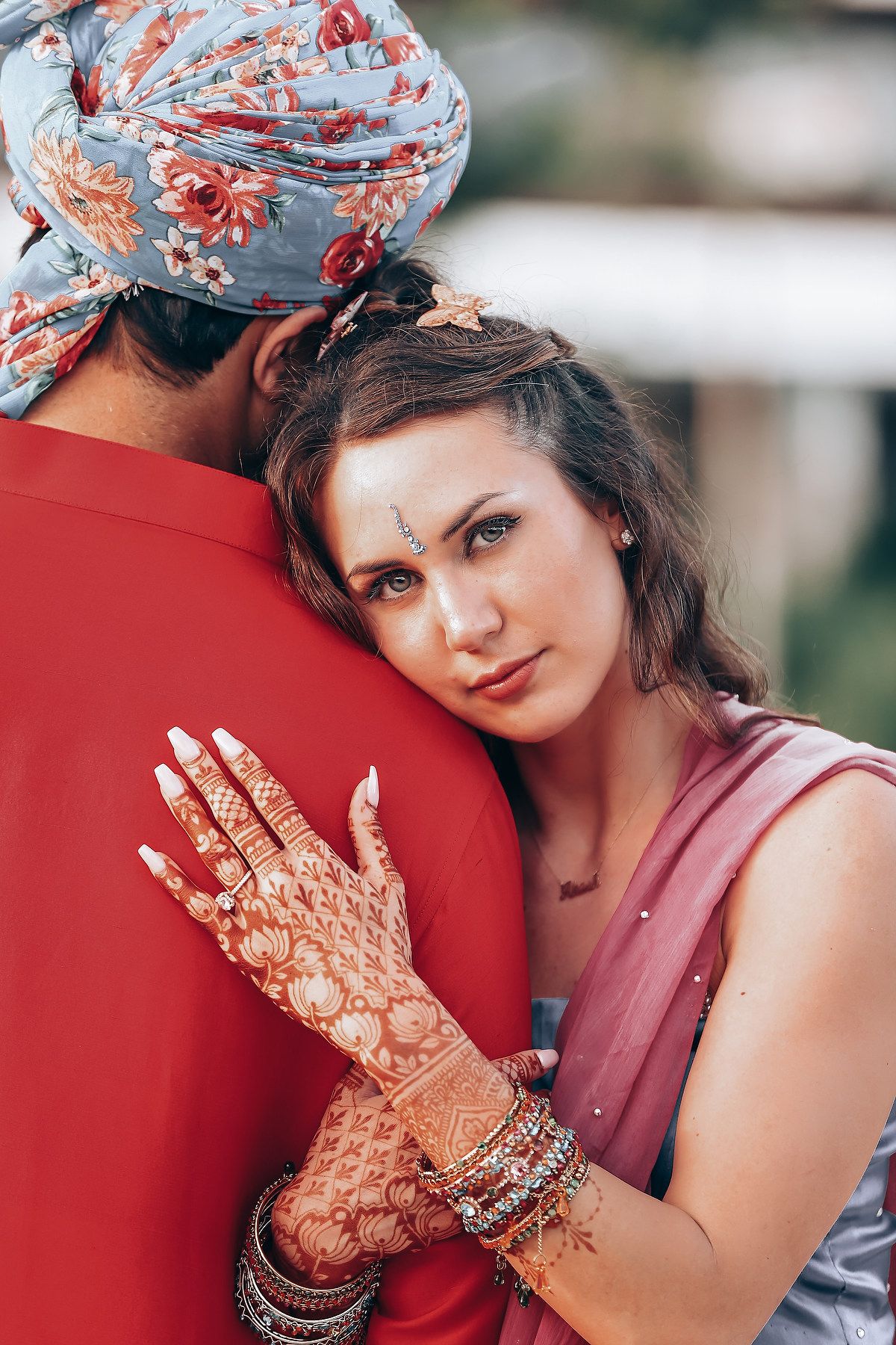 Woman wearing a floral headscarf and pink dress displays intricate henna designs on her hands.